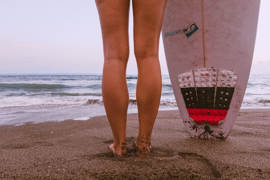 Barefoot surfer stands with board on sandy beach, ready for adventure