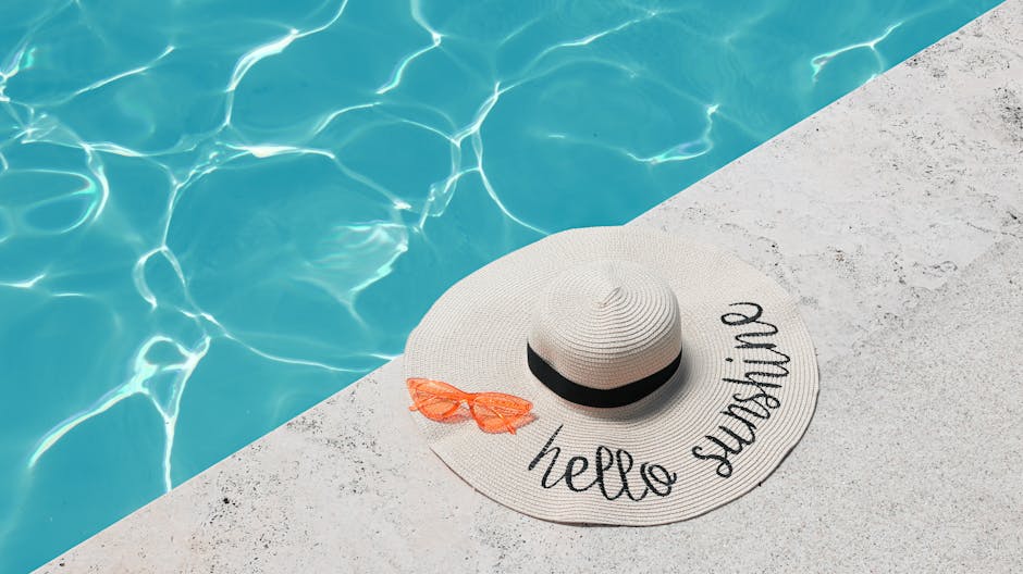 A sunhat with 'hello sunshine' and sunglasses by a shimmering pool on a summer day