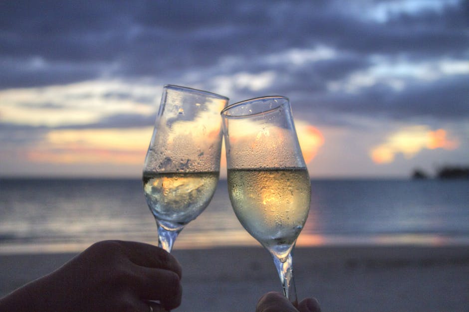 Two champagne glasses clink at sunset on a serene beach, evoking romance and celebration